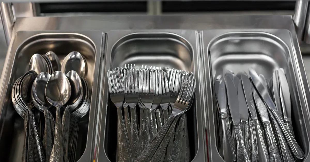 Stainless steel spoons, forks and knives in steel trays, typical food contact items covered by food contact materials compliance